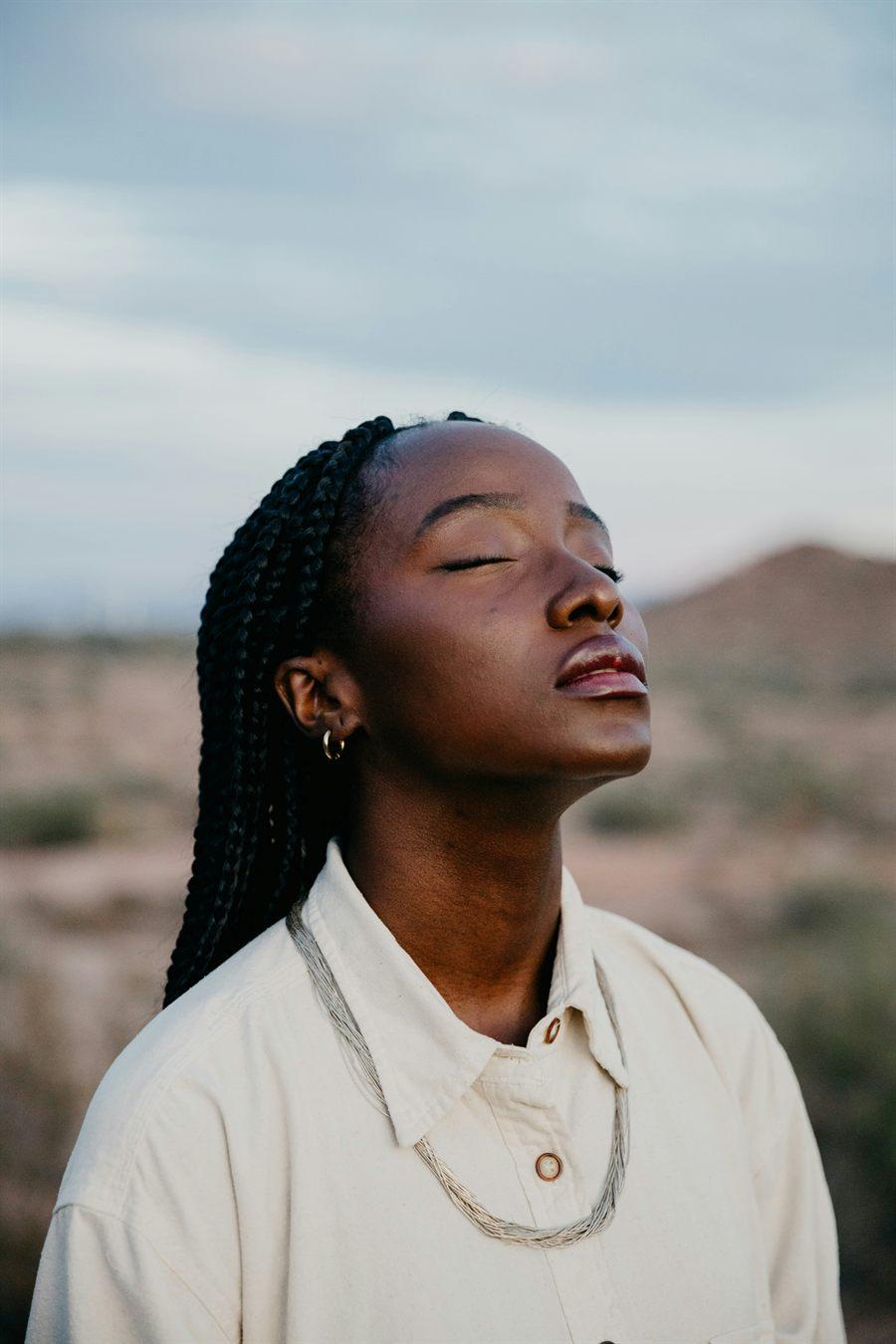 Mujer con trenzas respirando con los ojos cerrados al aire libre
