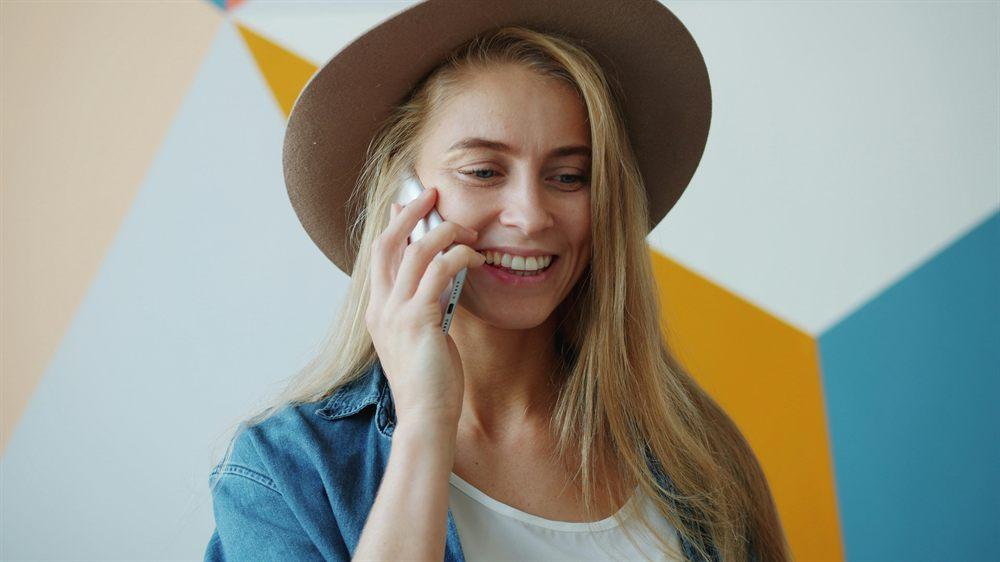 Mujer con sombrero sonriendo mientras habla por teléfono